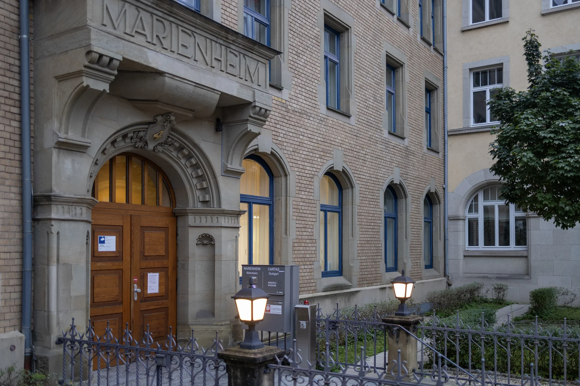 Historisches Backsteingebäude "Marienheim" mit Rundbogen-Eingang, blauen Fenstern und Straßenlaternen vor dem Eingang.